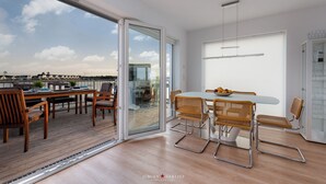 A modern dining area with a glass door leading to a balcony, a table with chairs, and a view of the cityscape. - Viktoria's Baltic Lounge - First row on the water, sauna, fireplace, balcony (Olpenitz)