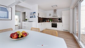 A modern kitchen with white cabinets, a central island, and a dining area with a table set for a meal. - Viktoria's Baltic Lounge - First row on the water, sauna, fireplace, balcony (Olpenitz)