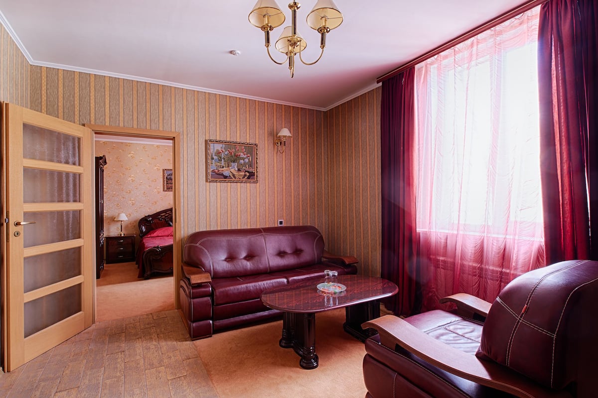 Una habitación con una pared revestida de madera, un sofá de cuero rojo, una pequeña mesa redonda y un ventanal con cortinas rojas.
