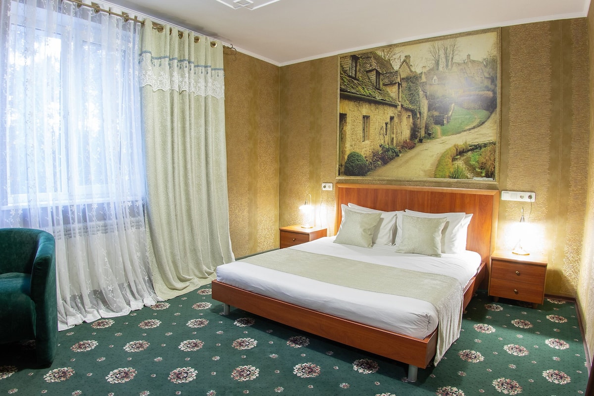 Habitación de hotel con cama, mesita de noche, lámpara, silla y un cuadro en la pared.