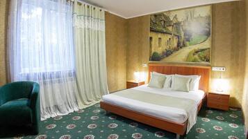 A hotel room with a bed, a nightstand, a lamp, a chair, and a painting on the wall.