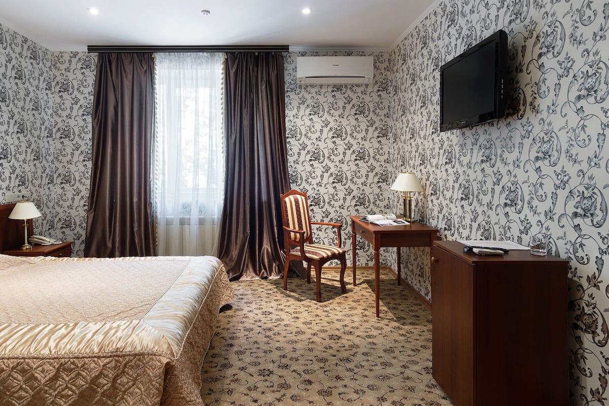 Habitación de hotel con cama, escritorio, silla, televisor y ventana con cortinas.