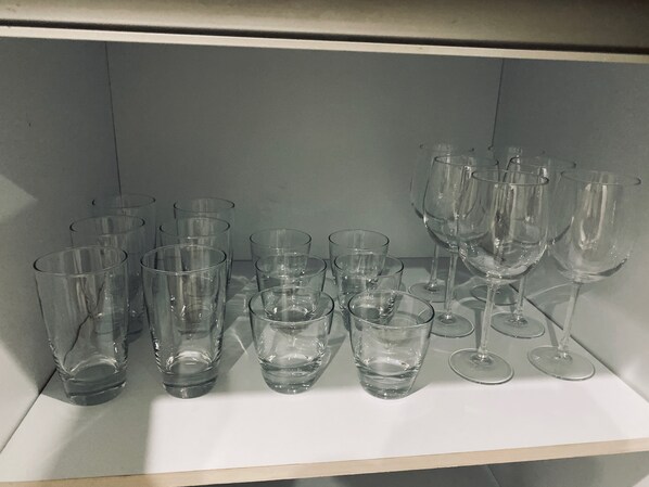 Una estantería con diferentes vasos de vidrio transparente, incluyendo varias copas de vino y varios vasos pequeños.