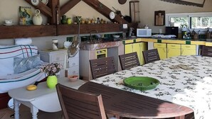 Maalaishenkinen keittiö, jossa on puupalkit, ruokapöytä tuoleineen sekä monenlaisia keittiövälineitä.