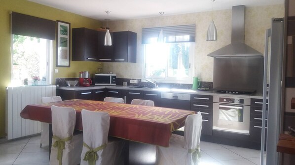 A modern kitchen with dark cabinets, a large stove, and a dining table set for four. - Beautiful quiet residential villa, large summer kitchen and private swimming pool (PIA)