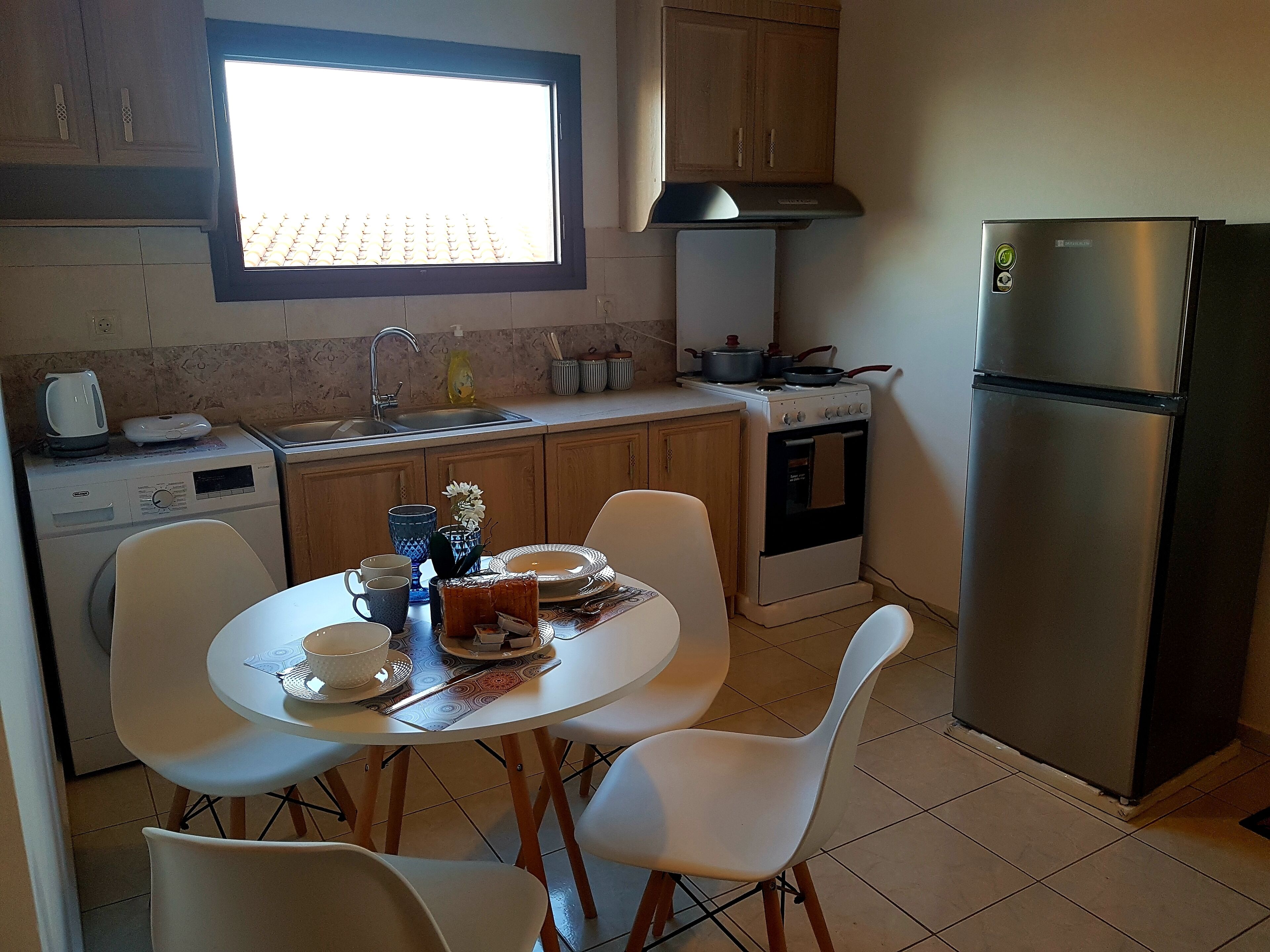 Una cocina compacta con mesa, sillas, refrigerador, estufa y lavadora.