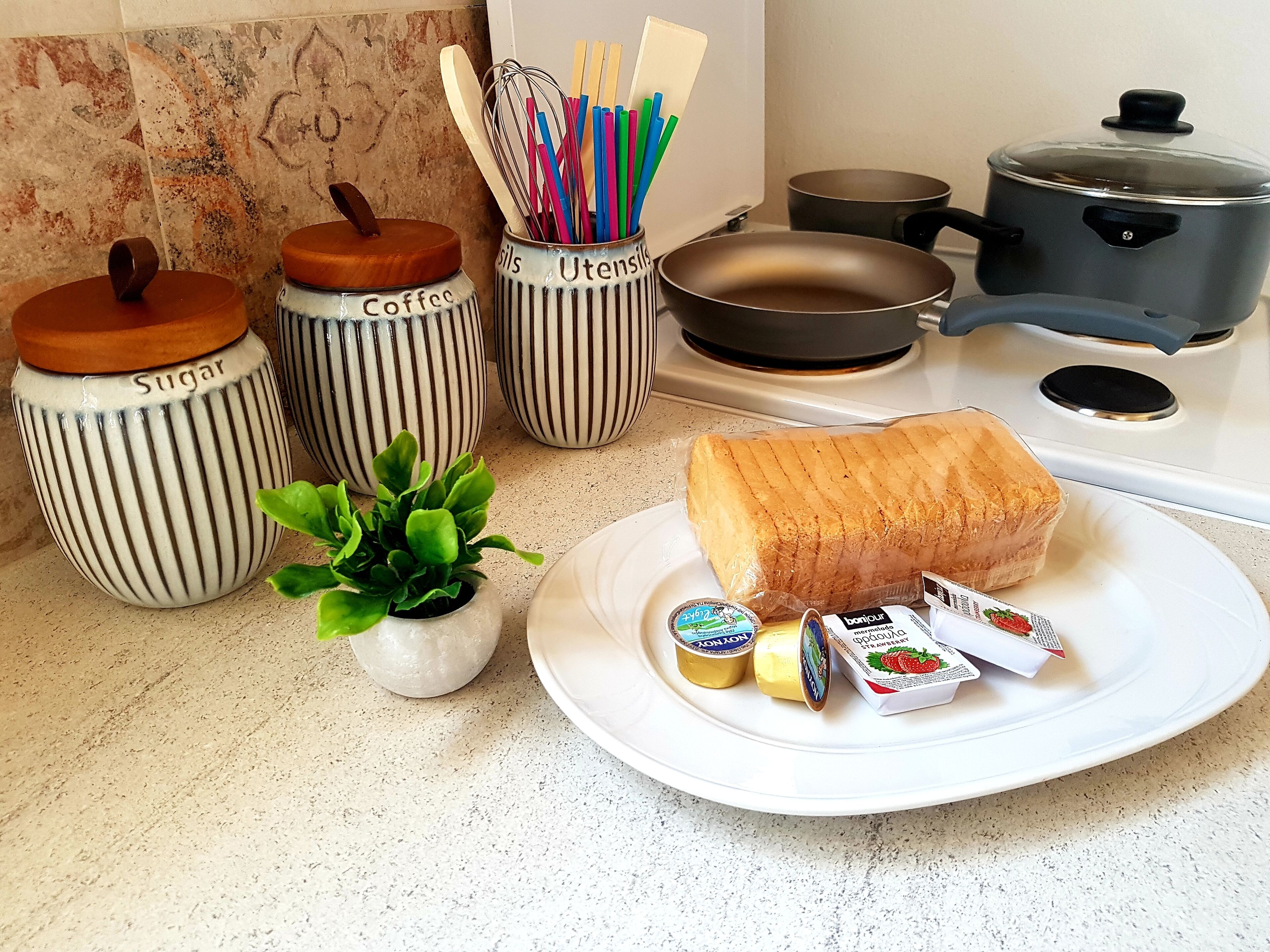 Een aanrecht met een brood, boter, jam en een kleine plant in een pot.