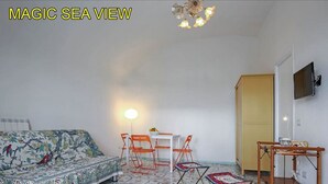 Ein Zimmer mit einem gemusterten Boden, einem Sofa mit floralem Bezug, einem Tisch mit Stühlen, einer Stehlampe, einem Fernseher und einem Holzschrank.