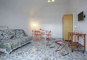 Une pièce avec un sol à motifs, un canapé recouvert d’un tissu à fleurs, une table avec des chaises, un lampadaire, un téléviseur et un meuble en bois.