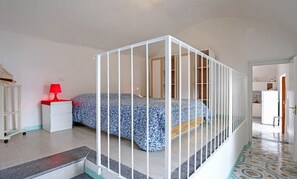 Une chambre à coucher avec un lit, une table de chevet blanche, une lampe rouge et une vue sur la mer par la fenêtre.