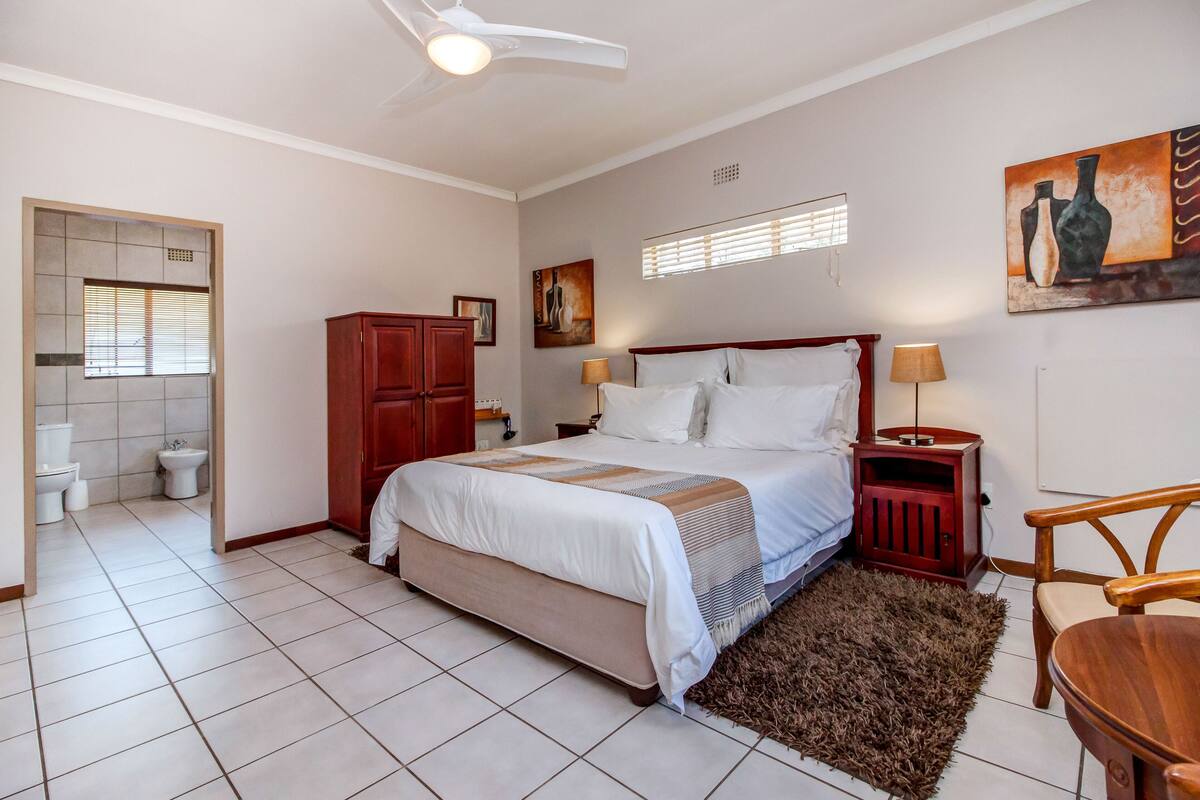 A bedroom with a bed, bedside table, lamp, and a painting on the wall.