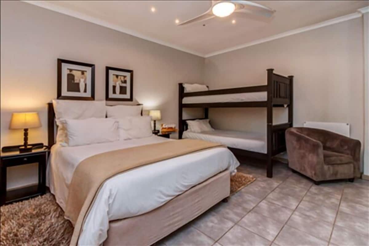 A bedroom with a large bed, two smaller beds, a chair, and a ceiling fan.