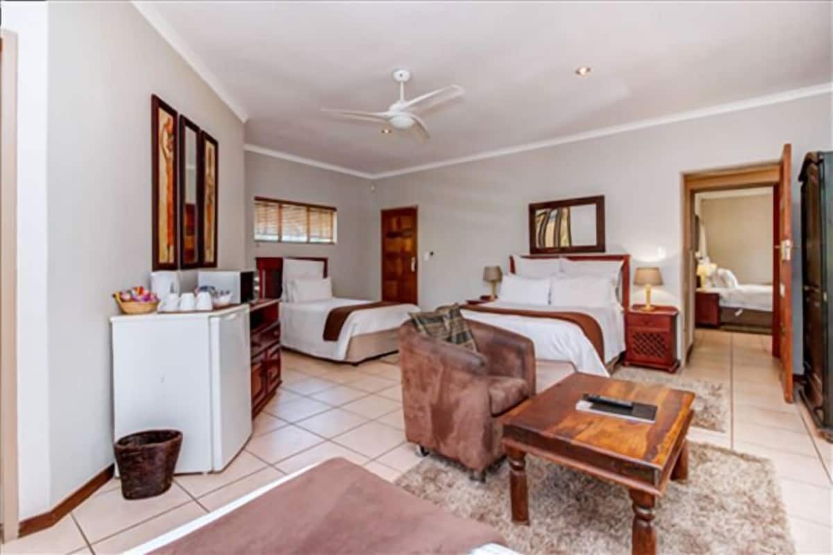 A hotel room with a bed, a desk, a chair, a small refrigerator, and a ceiling fan.