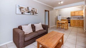 A living room with a brown sofa, a wooden coffee table, and a painting on the wall. - Dalberry Guest House (Sandton)