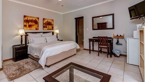 A hotel room with a bed, bedside lamps, a desk, a chair, a television, and a refrigerator. - Dalberry Guest House (Sandton)