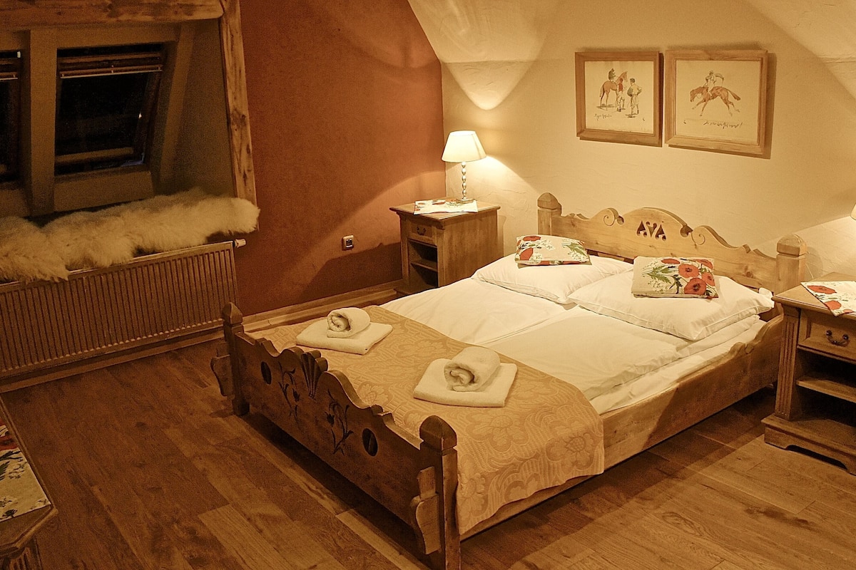 A cozy bedroom with a wooden bed, two bedside tables with lamps, a radiator, and two framed pictures on the wall.