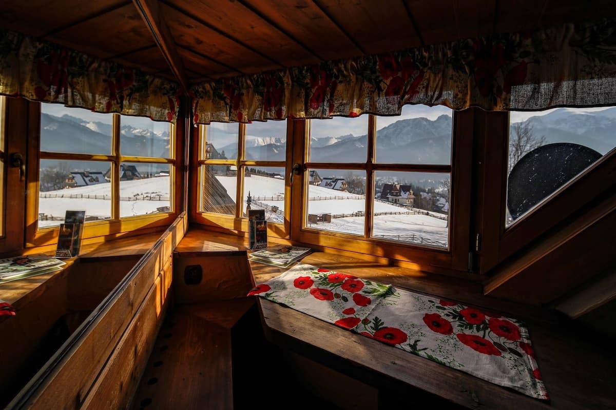 A cozy room with wooden walls and large windows offering a view of a snowy landscape and mountains.