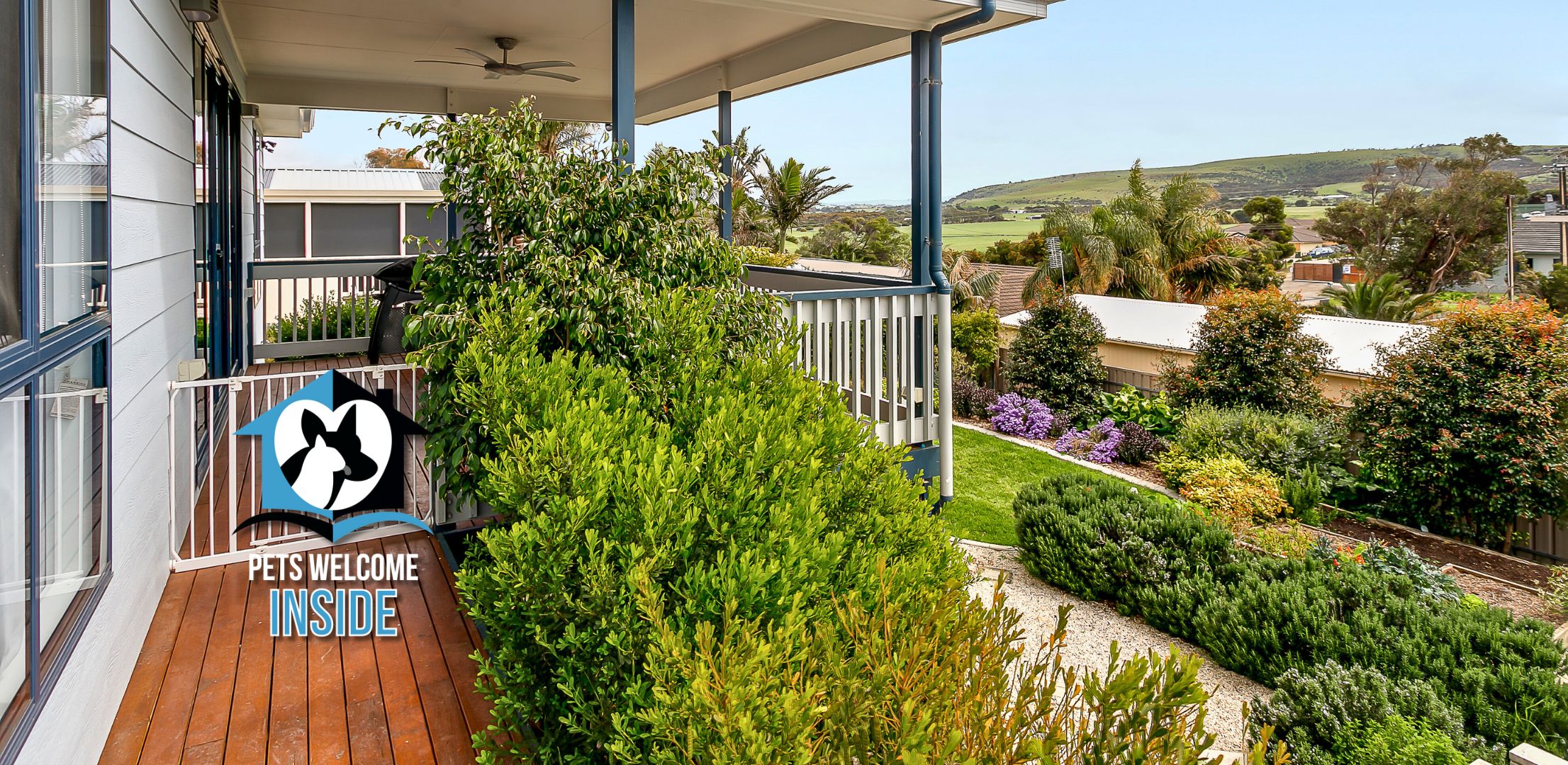A balcony with a 'Pets Welcome Inside' sign, surrounded by lush greenery and a view of a residential area.