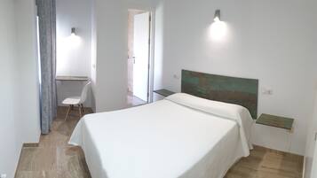 Un dormitorio con cama, escritorio y silla. Hay dos luces fijadas a la pared.