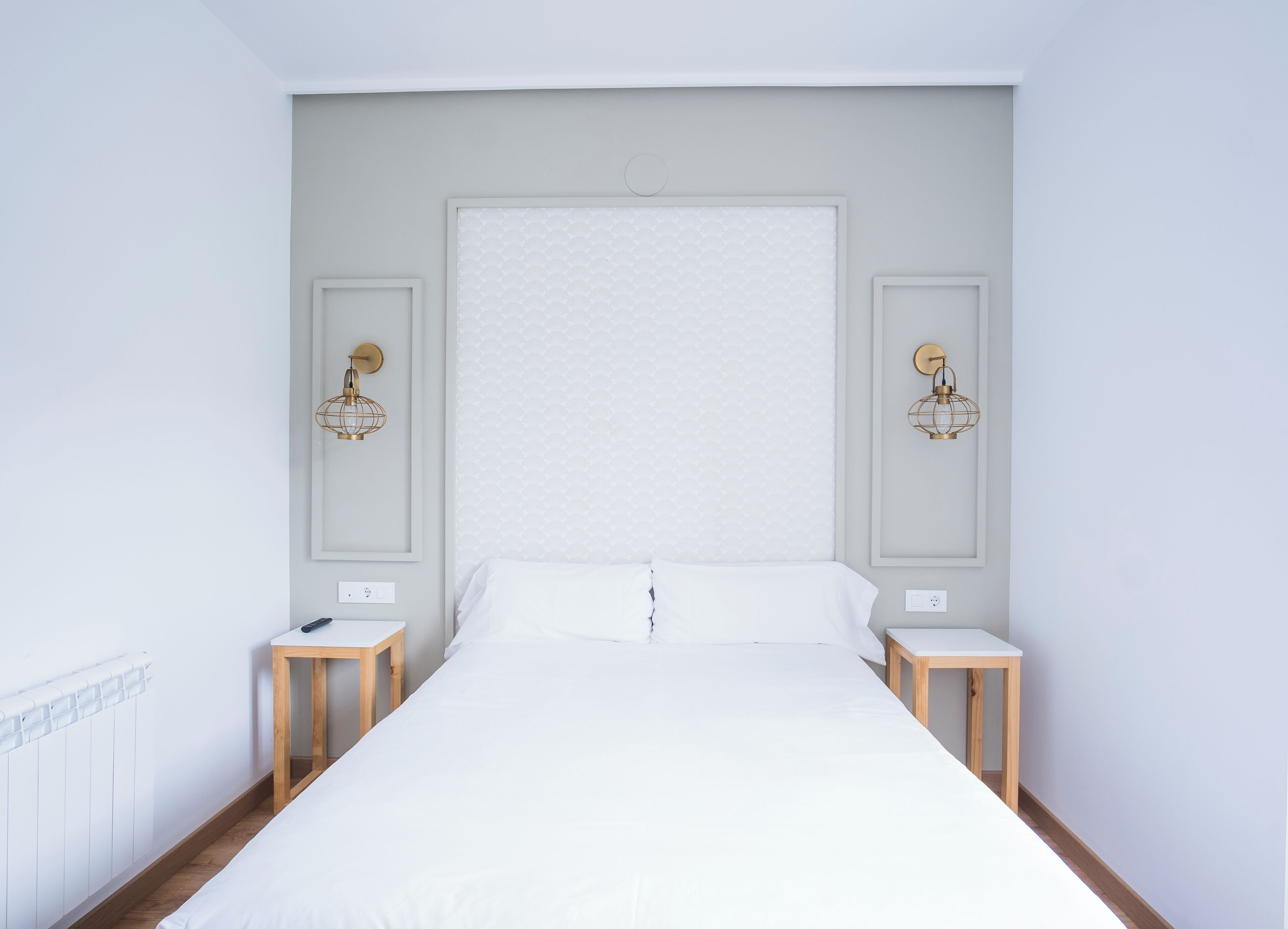Un dormitorio minimalista con una cama grande, dos mesitas de noche e iluminación empotrada en la pared.