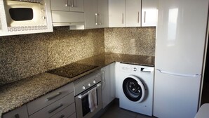 A compact kitchen with a microwave, oven, washing machine, and refrigerator.