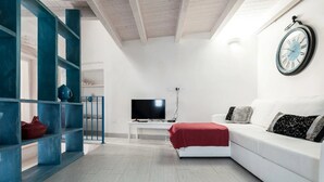 Un salon moderne avec un canapé blanc, un plaid rouge, un téléviseur et une horloge au mur.