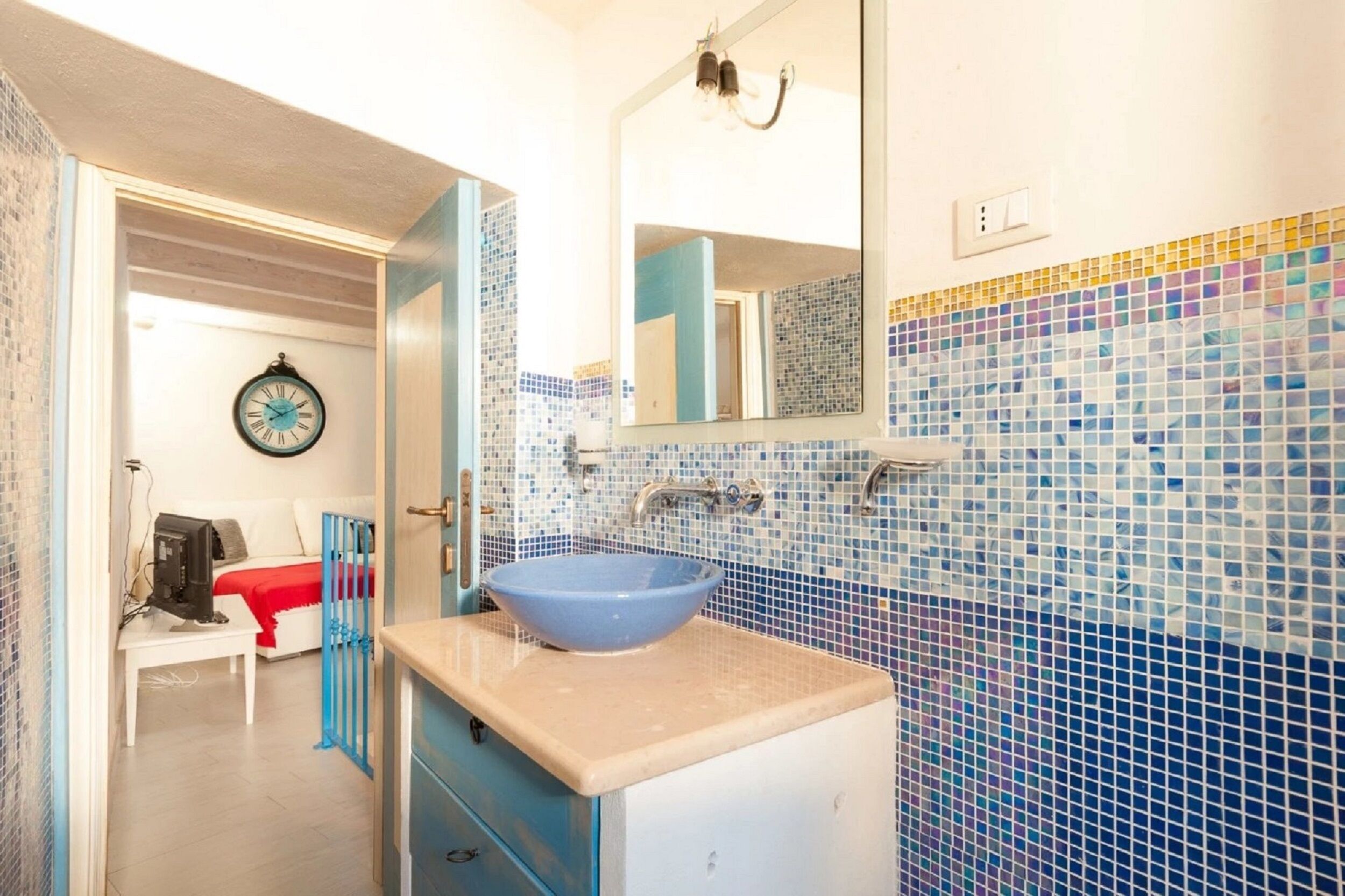 A bathroom with a blue sink, a mirror, and a tiled wall.