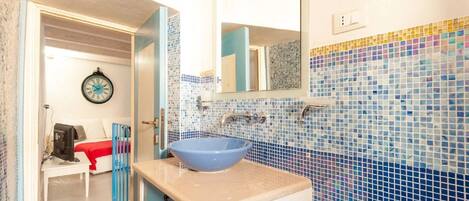 A bathroom with a blue sink, a mirror, and a tiled wall.