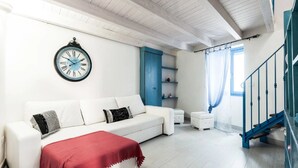 Un salon moderne avec un canapé blanc, un plaid rouge, une horloge, une porte bleue et un escalier avec des rampes bleues.