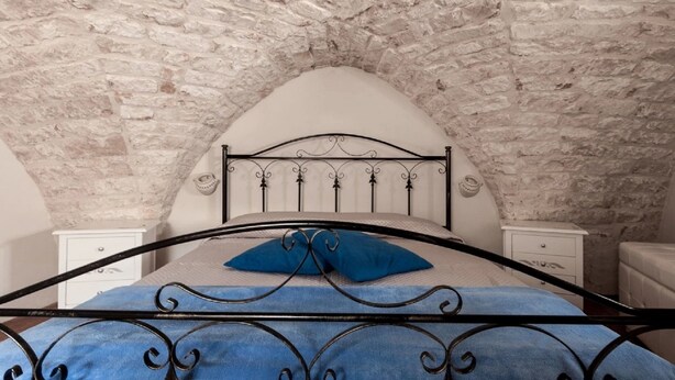 Une chambre avec un plafond en pierre, un cadre de lit en métal et deux tables de chevet.
