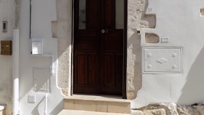 Un bâtiment blanc avec une porte en bois foncé, une petite fenêtre et un coffret électrique fixé au mur.