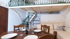 Un coin repas avec une table en bois dressée pour deux personnes, un escalier et un canapé blanc en arrière-plan.