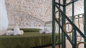 Une pièce avec un mur en pierre, un lit recouvert d’un tissu vert et agrémenté de serviettes blanches, et une rambarde en métal.