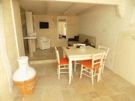 Een eetgedeelte met een tafel en stoelen, een witte vaas, en een trap naar een andere kamer.
