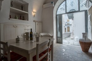 A dining area with a table set for two, a white chair, and a large vase. There is a shelf with decorative items above the table. - Casa Daniele (Ostuni)