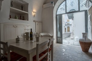 Een eetruimte met een tafel gedekt voor twee personen, een witte stoel en een grote vaas. Daarboven hangt een plank met decoratieve objecten.