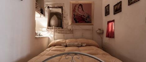 A bedroom with a metal bed frame, a wall-mounted shelf with decorative items, and a framed picture above the bed.