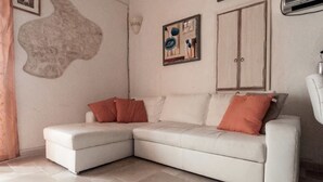 Ein Ecksofa mit heller Polsterung, ergänzt durch zwei rote Kissen, ein großes abstraktes Kunstwerk an der Wand und ein Kleiderschrank mit Doppeltüren.