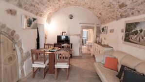 A cozy room with a stone ceiling, a dining table with chairs, a television, and a sofa with cushions. - Biancocalce (Ostuni)