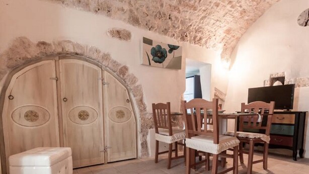 A room with a large arched doorway, wooden chairs, a small table, and a cabinet. - Biancocalce (Ostuni)