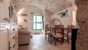 A rustic room with a stone ceiling, a wooden dining table with chairs, a white sofa, and a dresser. - Biancocalce (Ostuni)