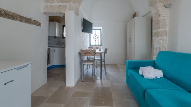 A compact living space with a dining area, a teal sofa, and a kitchen visible in the background. - Casina Nina (Ostuni)
