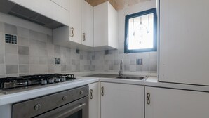 A kitchen with white cabinets, a gas stove, an oven, and a window with a view. - Casina Nina (Ostuni)