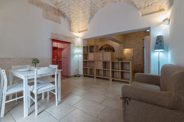 A dining area with a white table and chairs, a wooden cabinet, and a sofa. - Biancanicchia (Ostuni)