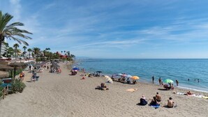 Une plage où l’on peut se détendre au soleil et se baigner, avec des palmiers et un ciel dégagé.