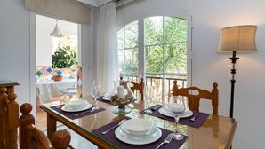 Un coin repas avec une table dressée pour deux personnes, une lampe et une vue sur la verdure à l’extérieur.