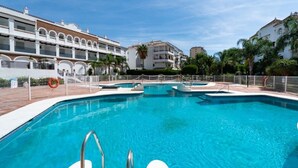Une piscine dotée de plusieurs couloirs, entourée d’une clôture et située à côté d’un immeuble à plusieurs étages avec des balcons.