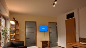 Una sala de estar con un sofá, un televisor montado en la pared, una mesita y un mueble con puertas de cristal.