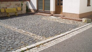 Un edificio con un patio empedrado de piedra, un banco de madera y una puerta con paneles de vidrio.