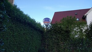 Un globo aerostático con un logotipo y texto visibles, volando sobre un edificio rodeado de follaje denso.